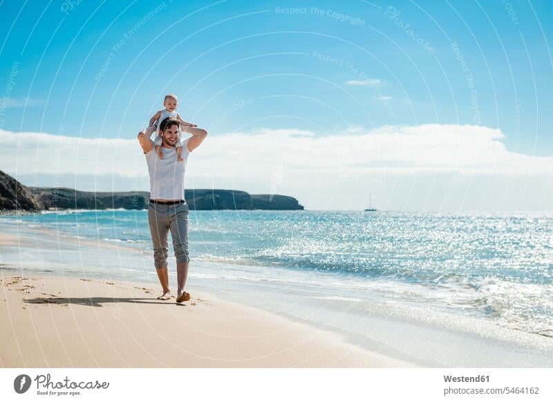 Spain, Lanzarote, father carrying little daughter on his shoulders on the beach daughters fathers daddy dads papa beaches baby infants nurselings babies child