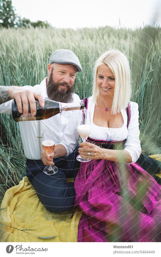 Man pouring champagne in glass held by woman while sitting amidst plants on land color image colour image Austria outdoors location shots outdoor shot