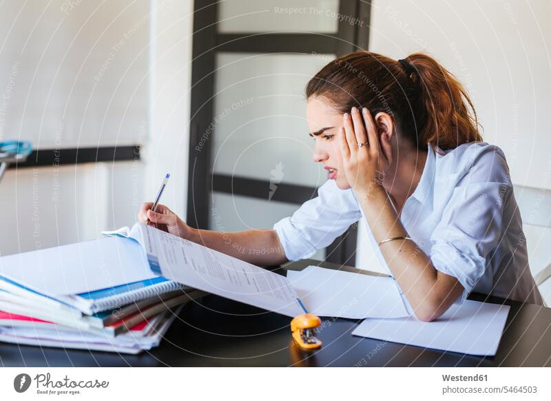 Frustrated female student with documents at desk at home Tables desks pencil pencils pens learn read Seated sit study Emotions Feeling Feelings Sentiment