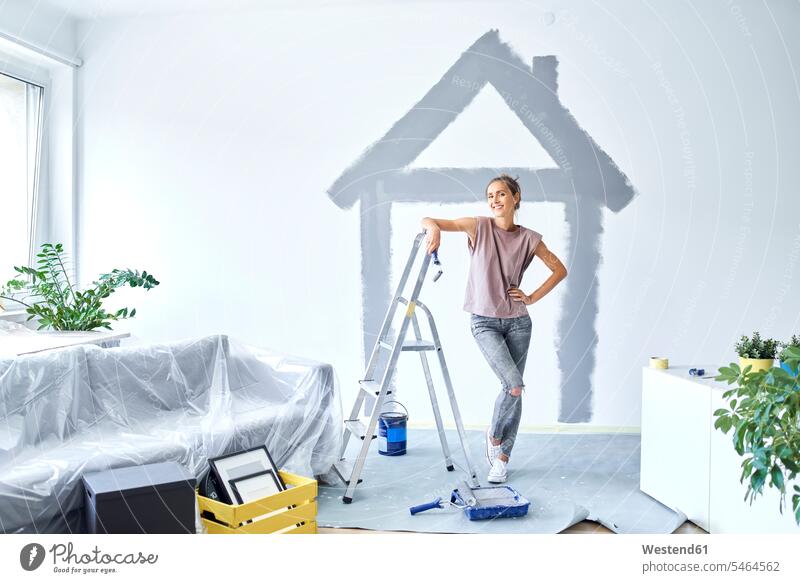 Smiling woman with hand on hip standing against house painted on wall at home color image colour image indoors indoor shot indoor shots interior interior view