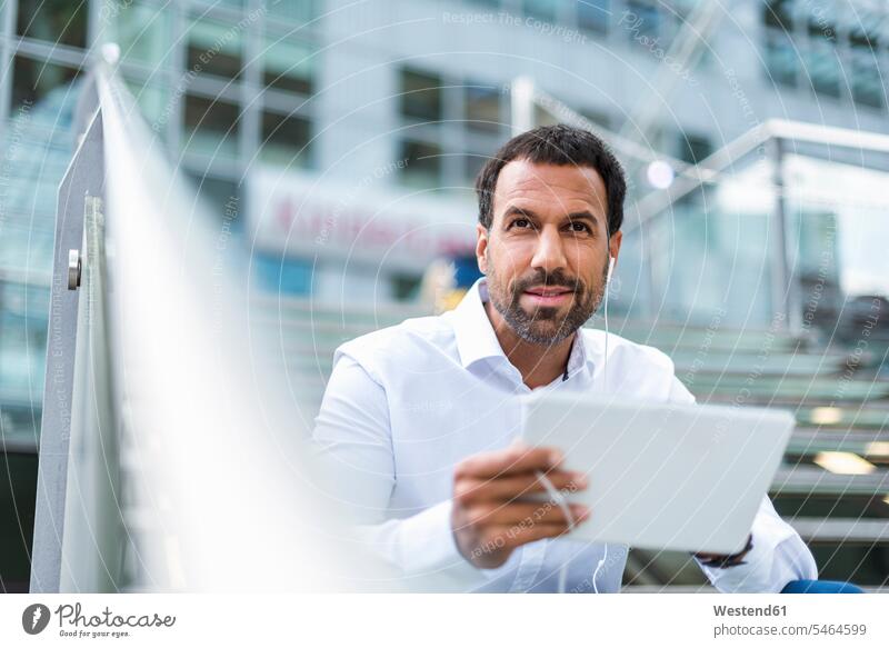 Businessman using tablet, earphones sitting Seated Business man Businessmen Business men portrait portraits males wireless Wireless Connection