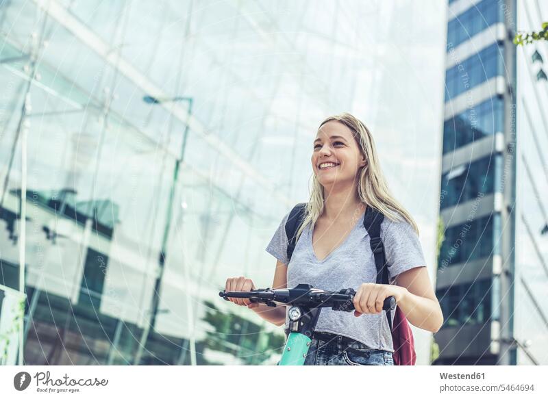 Portrait of laughing young woman with E-Scooter in the city, Berlin, Germany back-pack back-packs backpacks rucksack rucksacks drive smile seasons summer time