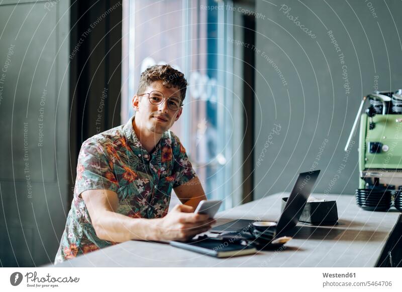 Young man sitting in cafe, using samrtphone and laptop human human being human beings humans person persons caucasian appearance caucasian ethnicity european 1