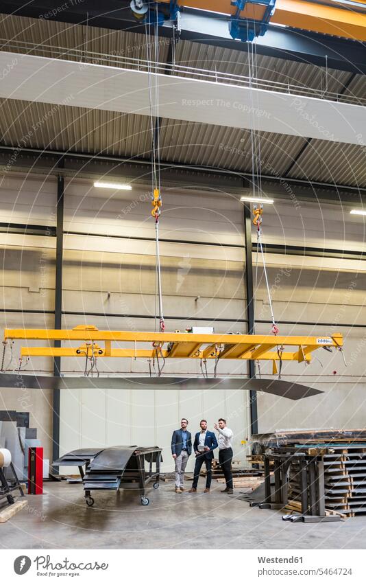 Three men standing on factory shop floor factories production hall man males Adults grown-ups grownups adult people persons human being humans human beings