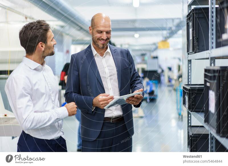 Smiling businessman using digital tablet while listening to engineer during discussion at industry color image colour image indoors indoor shot indoor shots