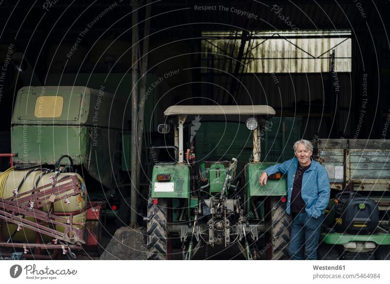 Portrait of a confident senior man on a farm with tractor in barn agriculturist agriculturists farmers shirts motor vehicles road vehicle road vehicles tractors