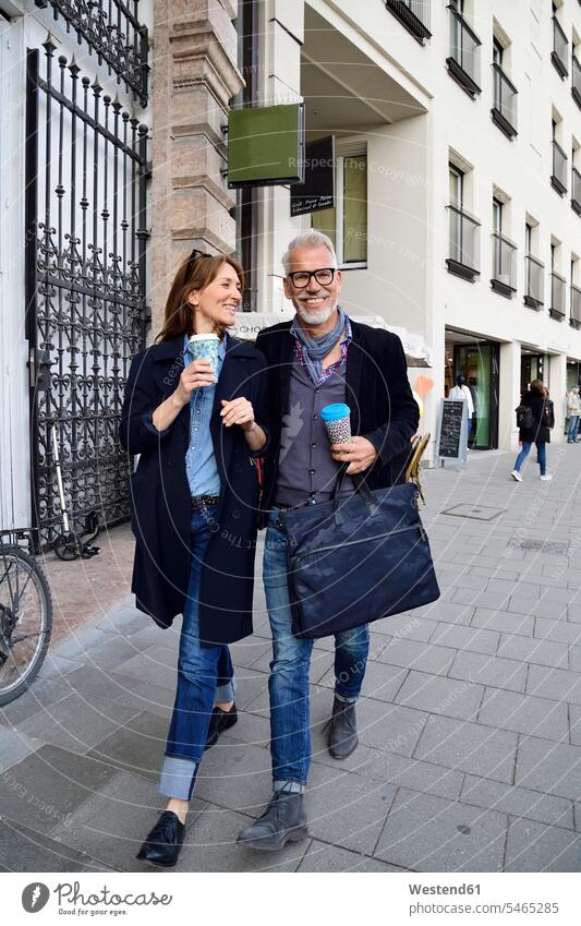 Smiling mature couple with reusable bamboo cups walking in the city Munich reuse re-usable female tourist Coffee to Go takeaway coffee shopping spree