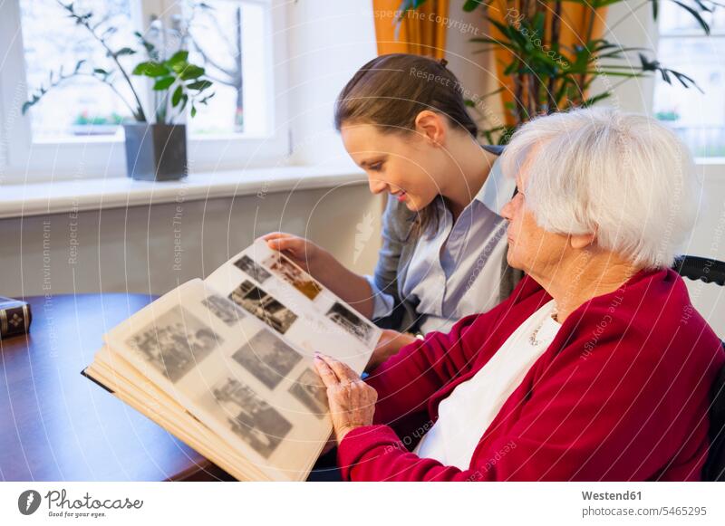 Grandmother and granddaughter looking photo album at home color image colour image Germany indoors indoor shot indoor shots interior interior view Interiors