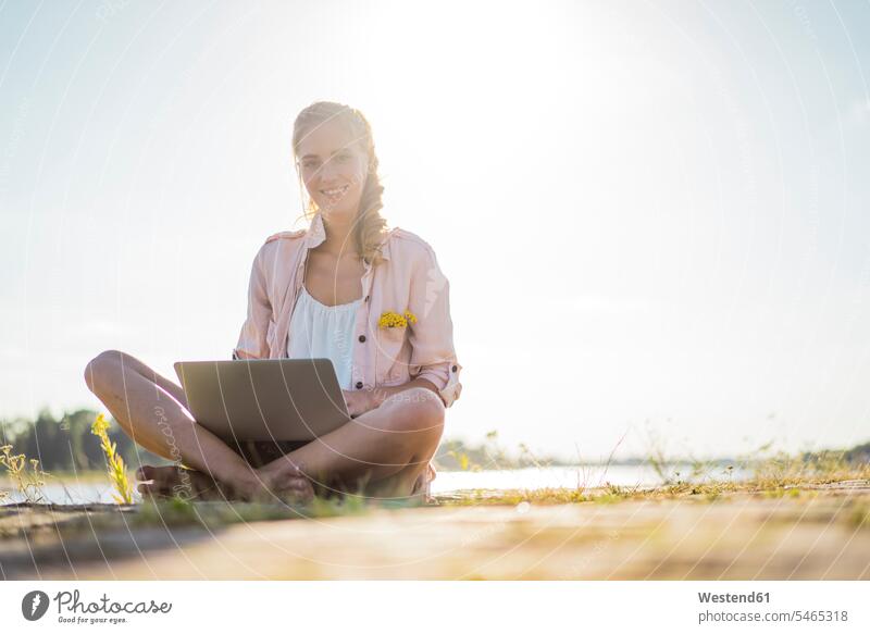 Portrait of smiling woman sitting at the riverside in summer using laptop portrait portraits River Rivers summer time summery summertime Laptop Computers