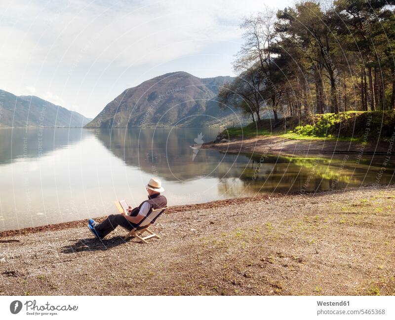 Italy, Lombardy, senior man sitting at Lake Idro using tablet senior men elder man elder men senior citizen Seated digitizer Tablet Computer Tablet PC