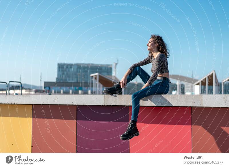 Young woman siiting on a wall, looking over city smiling smile walls red young women young woman summer summer time summery summertime sitting Seated females