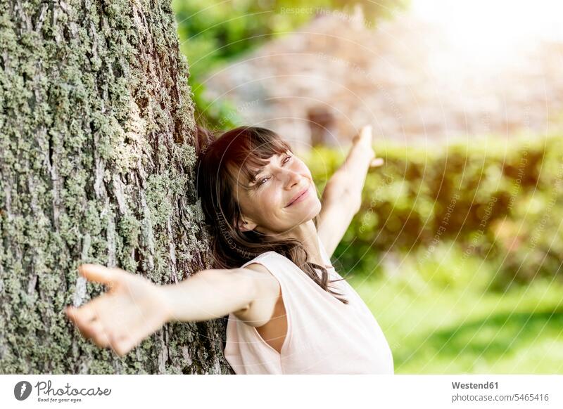 Portrait of smiling brunette woman leaning against a tree trunk human human being human beings humans person persons caucasian appearance caucasian ethnicity