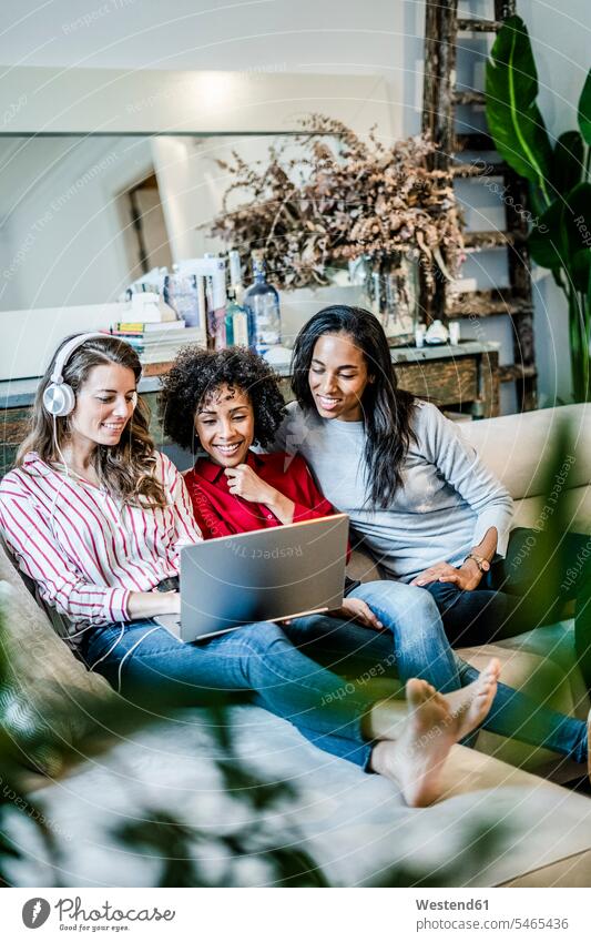 Three happy women with laptop sitting on couch Seated woman females happiness Laptop Computers laptops notebook settee sofa sofas couches settees female friends