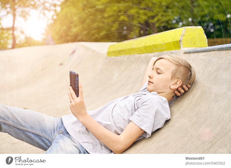 Boy using smartphone in skatepark leisure free time leisure time watching looking looking at eyeing lying laying down lie lying down boy boys males Smartphone