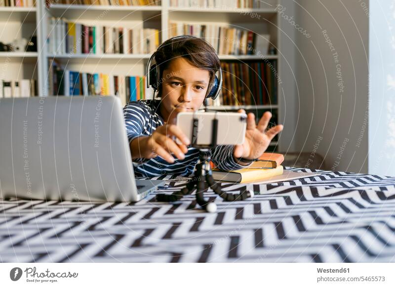 Boy adjusting smart phone on tripod sitting by laptop at table color image colour image 8-9 years 8 to 9 years children kid kids people human being human beings