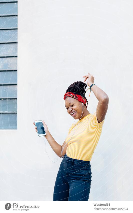 Young woman listening music with headphones and earphones singing and dancing in front of white wall T- Shirt t-shirts tee-shirt cell phone cell phones