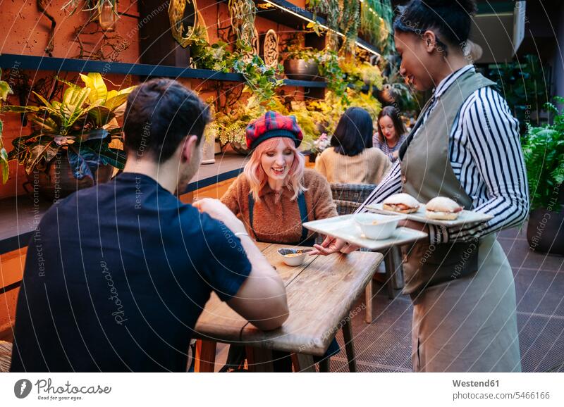 Waitress is serving food to couple, sitting in restaurant Wait Staff server waiters waitresses smile Seated drink enjoy enjoyment indulgence indulging savoring