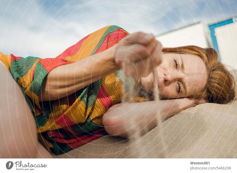 Redheaded woman lying on the beach, with sand trickling through her hand beaches redheaded red hair red hairs red-haired resting daydreaming day dreaming