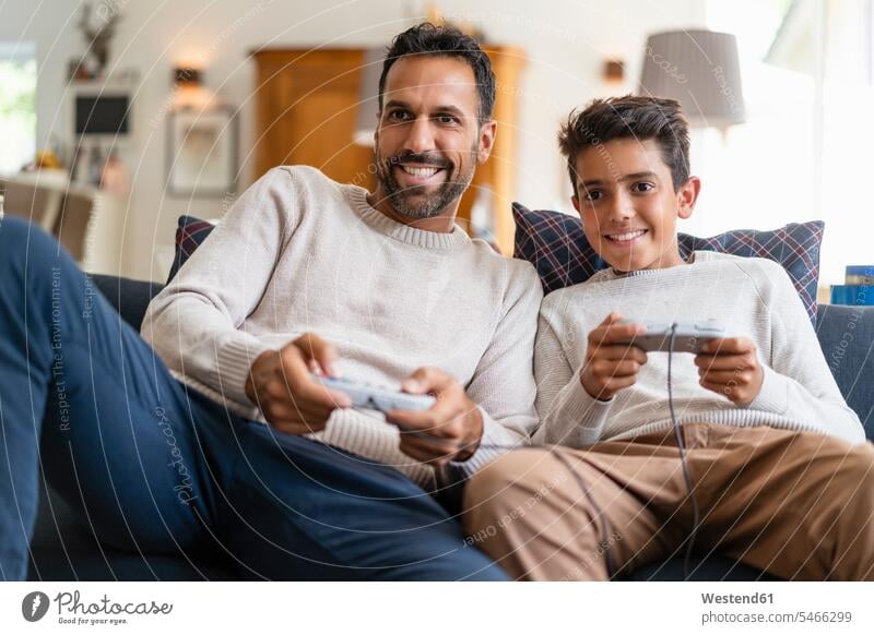 Happy father and son playing video game on couch in living room (value=0) human human being human beings humans person persons caucasian appearance