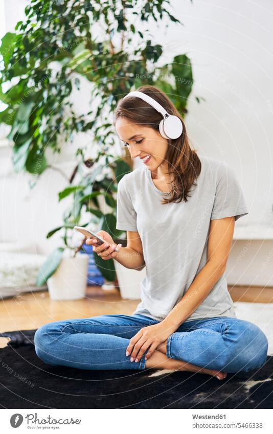 Smiling young woman sitting on the floor with headphones and cell phone headset mobile phone mobiles mobile phones Cellphone cell phones Seated females women