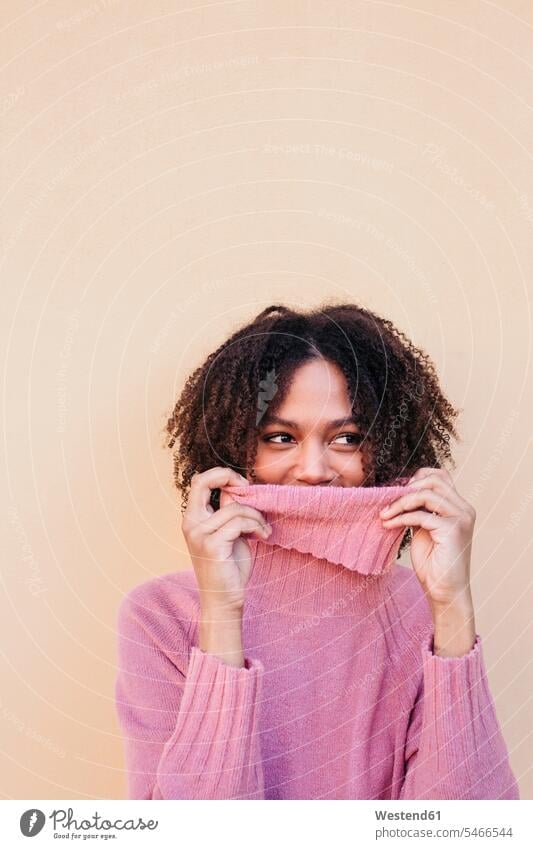 Portrait of smiling young woman wearing pink turtleneck pullover leaning against wall Rosy sweater jumper Sweaters females women portrait portraits colour