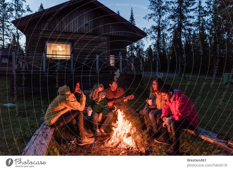 Group of friends sitting at a campfire, talking and playing guitar Camp Fire Campfire Bonfire making music playing music make music play music Fun having fun