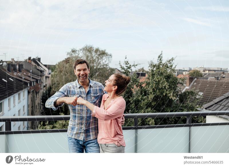 Cheerful mature couple's fist together while standing in balcony color image colour image outdoors location shots outdoor shot outdoor shots day daylight shot