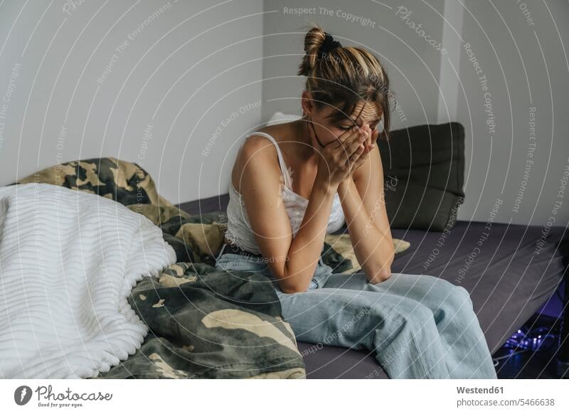 Despaired teenage girl sitting on bed, covering face with hands human human being human beings humans person persons Mixed Race mixed race ethnicity