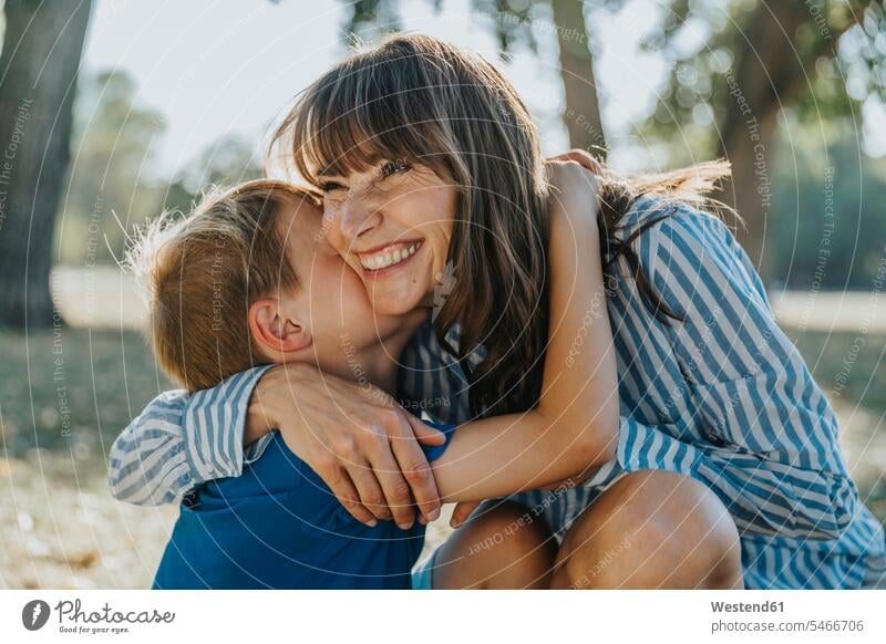 Smiling mother embracing son in public park color image colour image outdoors location shots outdoor shot outdoor shots day daylight shot daylight shots