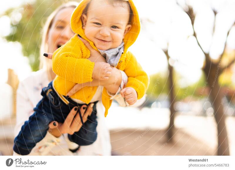 Happy mother playing with baby boy in a park coat coats jackets hold smile delight enjoyment Pleasant pleasure Cheerfulness exhilaration gaiety gay glad Joyous