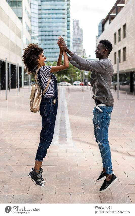 Happy couple jumping and high-fiving in the street Leaping laughing Laughter twosomes partnership couples High Five high fiving Hi-Five High-Five happiness