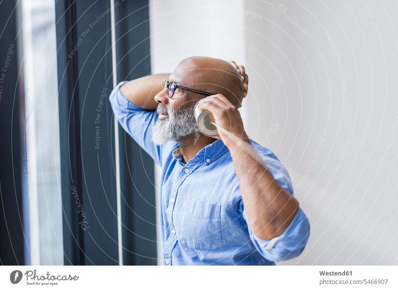 Businessman looking out of window while using tin can phone Tin Can Phone watching windows Business man Businessmen Business men use males view seeing viewing