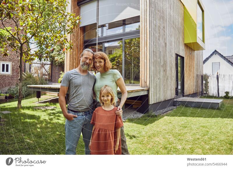 Smiling daughter standing with parents against tiny house in yard color image colour image Germany leisure activity leisure activities free time leisure time