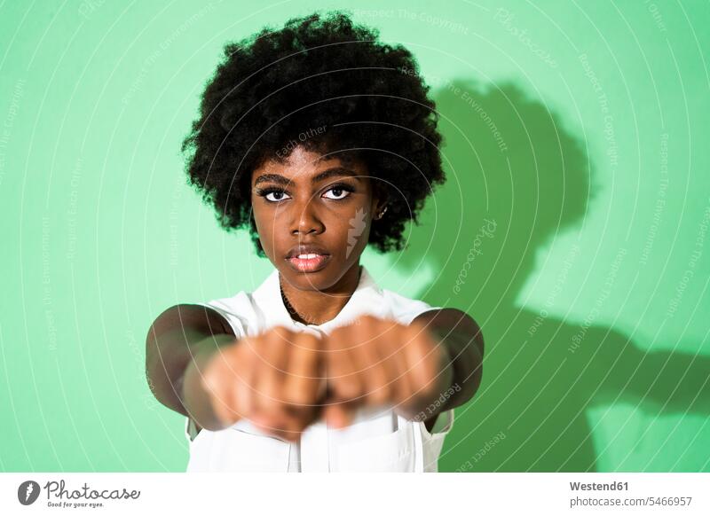 Young woman showing fist while standing against green background color image colour image studio shot studio photograph studio photographs studio shots indoors