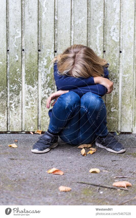 Sad girl crouching in front of wooden wall hiding her face sad hide wooden walls females girls cowering Emotion Feeling Feelings Sentiments Emotions emotional