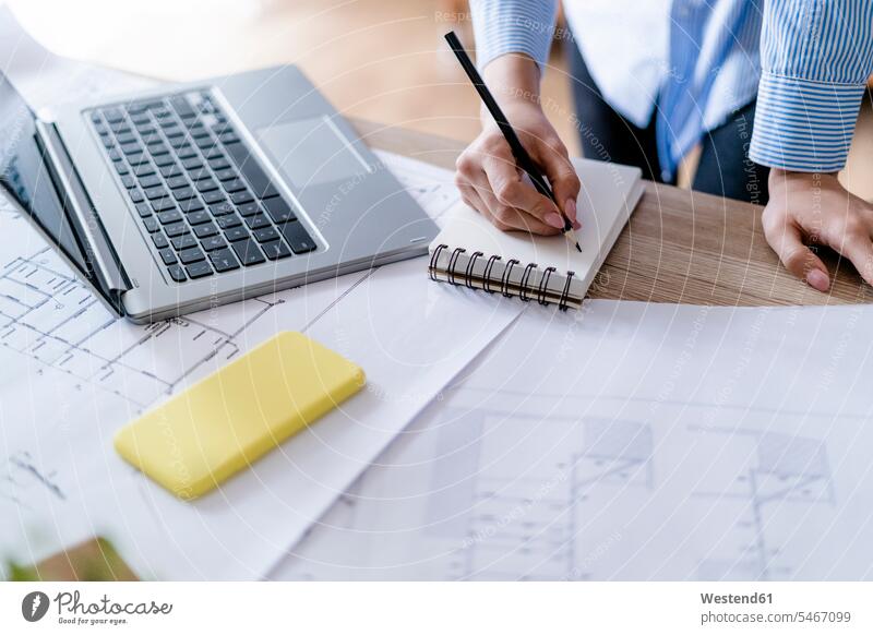 Close-up of woman in office taking notes with plan and laptop on table human human being human beings humans person persons caucasian appearance