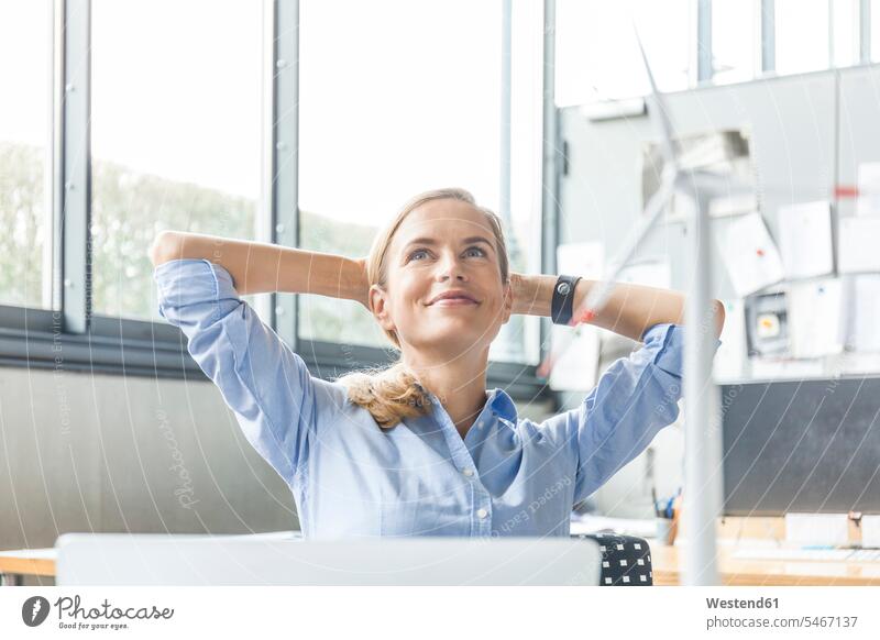 Smiling woman in office with wind turbine model in foreground smiling smile models females women offices office room office rooms wind wheel windmills