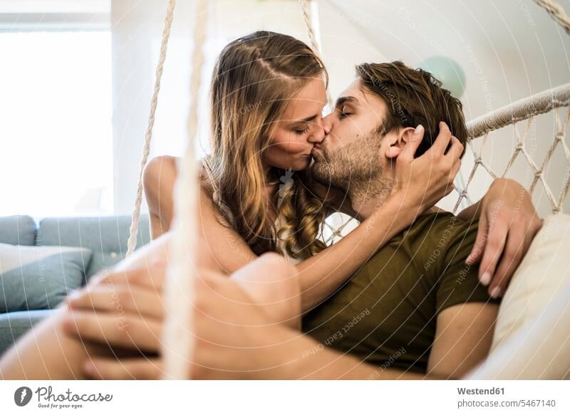 Affectionate couple kissing in hanging chair at home Swinging Chair hanging chairs Swinging Chairs kisses twosomes partnership couples people persons