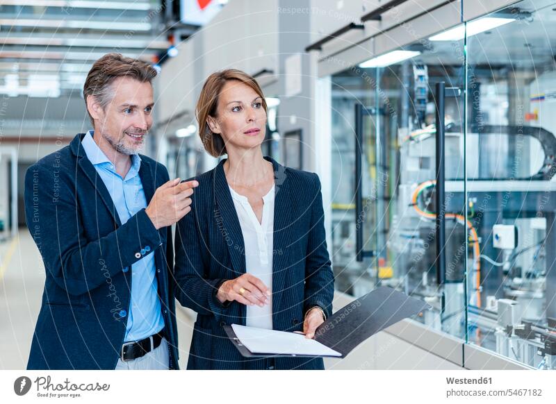 Businessman and businesswoman talking in a modern factory hall business life business world business person businesspeople associate associates