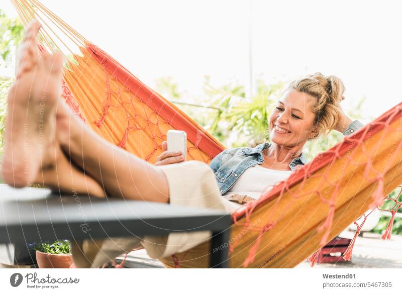 Portrait of happy mature woman hammocks Tables telecommunication phones telephone telephones cell phone cell phones Cellphone mobile mobile phones mobiles relax