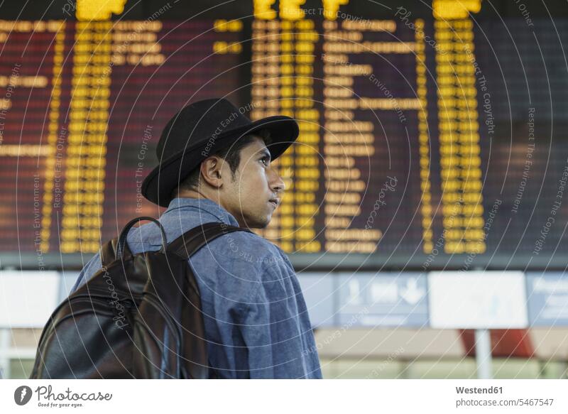 Young man with hat and backpack at arrival departure board at the airport departures board Arrival Departure Board rucksacks backpacks back-packs terminal