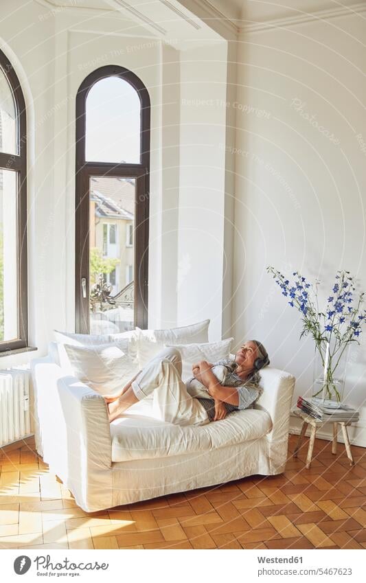 Thoughtful woman listening to music on sofa in living room Germany indoors indoor shot indoor shots interior interior view Interiors day daylight shot