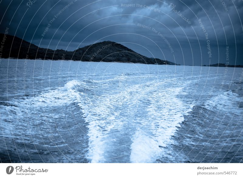 Dark clouds in the background . With fast speed the motorboat drives away from the island You can see a strong bow wave on the water. Thunderstorm atmosphere