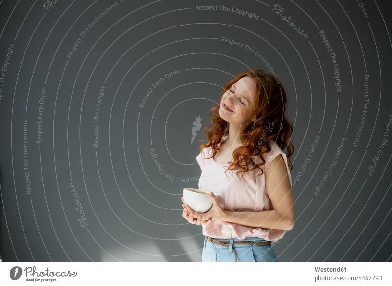 Portrait of happy redheaded woman with coffee bowl against grey background Crockery Tableware Bowls relax relaxing smile relaxation delight enjoyment Pleasant