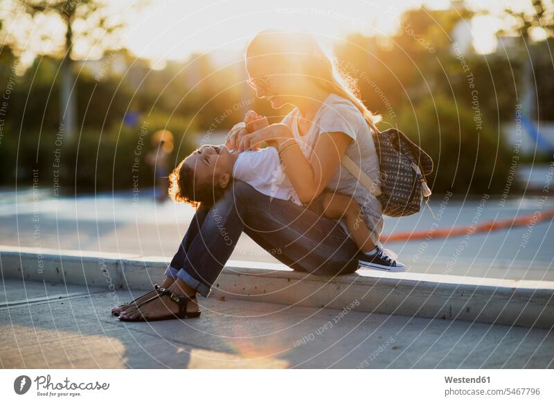 Happy mother playing with her little son on a square at sunset sons manchild manchildren plaza places Public Square happiness happy mommy mothers mummy mama