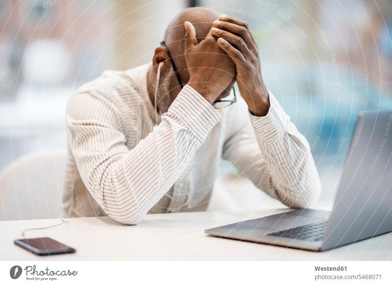 Mature businessman with earphones, smartphoen and laptop sitting with hands on head at desk Businessman Business man Businessmen Business men Smartphone iPhone