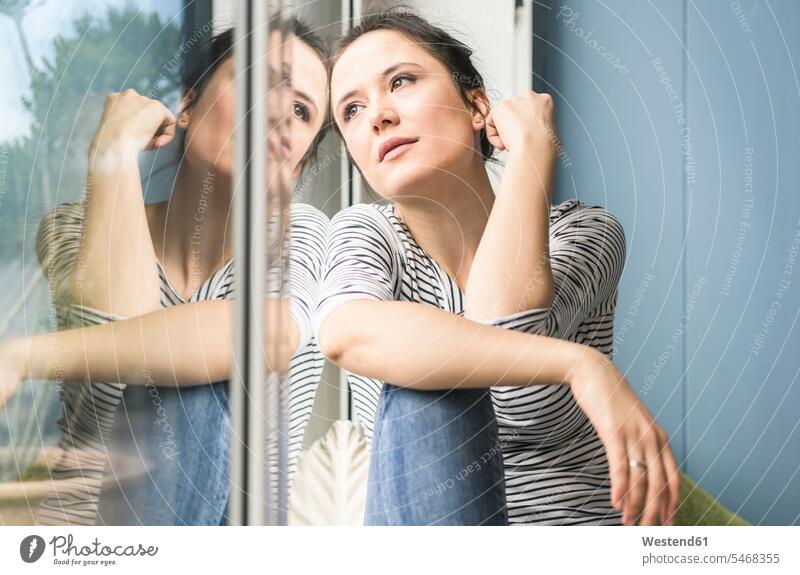 Serious woman looking out of window at home windows view seeing viewing sitting Seated serious earnest Seriousness austere females women Adults grown-ups