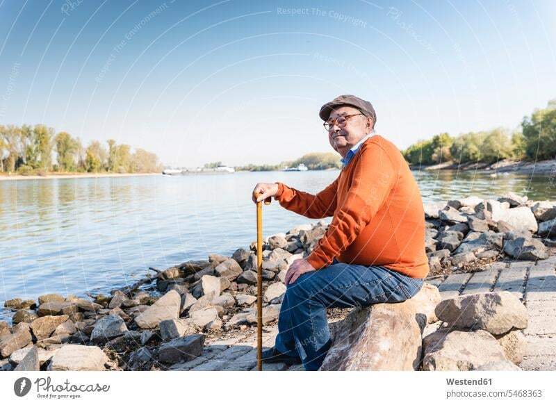 Old man sitting by the river confidence confident River Rivers Seated cap caps riverside riverbank watching observing observe senior men senior man elder man