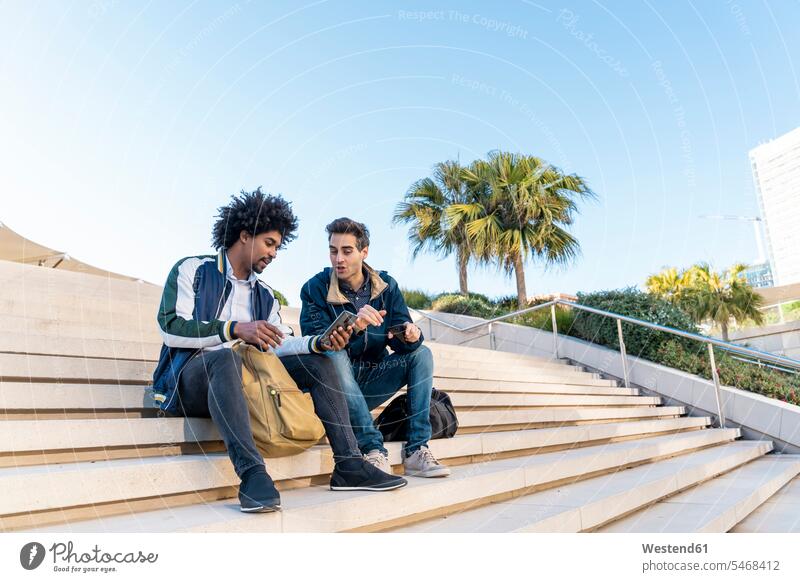 Two casual businessmen sitting on stairs sharing cell phone human human being human beings humans person persons caucasian appearance caucasian ethnicity