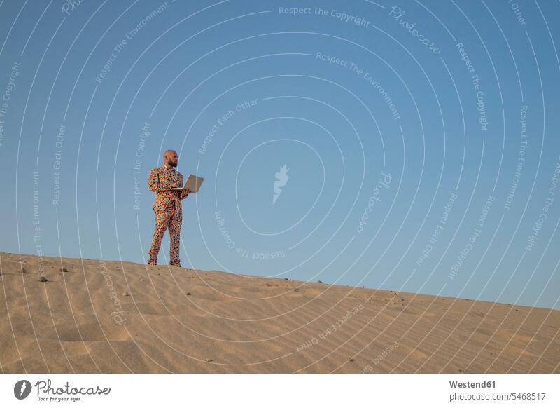 Man with laptop wearing suit with colourful polka-dots standing on sand dune looking at distance sand dunes Polka Dot Polka Dots Polka-Dot Polka-Dots colorful